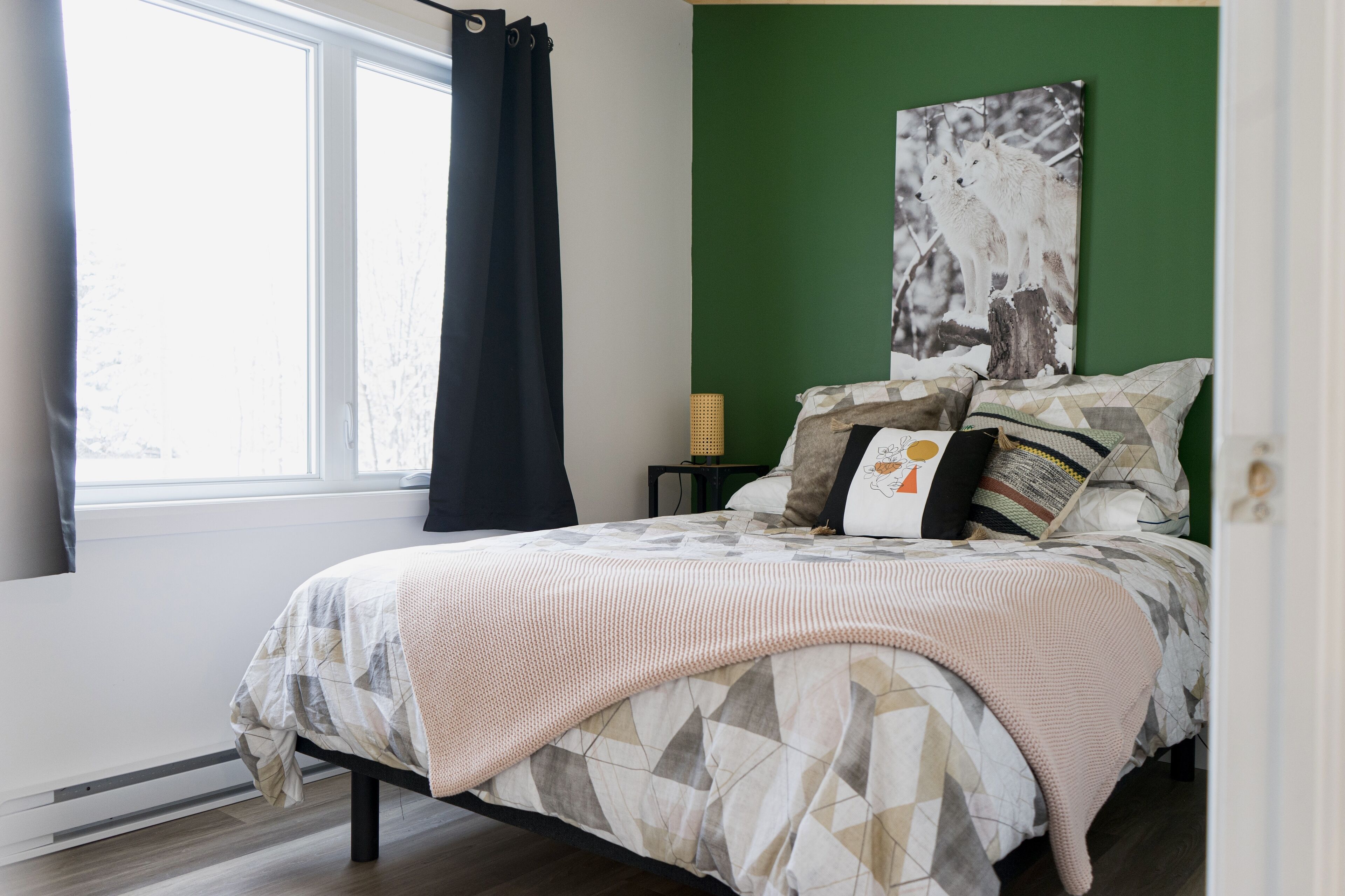 A bedroom with a bed, a green accent wall, and a window with curtains.