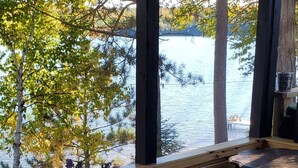 Une table recouverte d’une nappe à carreaux, une plante en pot et une vue sur un lac, visible à travers de grandes fenêtres.