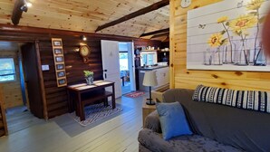 L’intérieur d’un chalet confortable, avec des murs en bois, une table à manger en bois, un canapé et un coin cuisine visible à travers une porte ouverte.