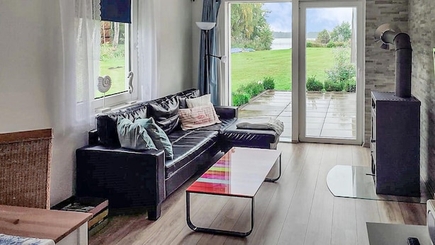 A modern living room with a black leather sofa, a glass coffee table, and a view of a garden through large sliding glass doors. - Lake front home in Heidesee with WiFi (Heidesee)