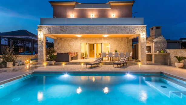 Une maison moderne à deux étages, dotée d’une piscine, d’un espace extérieur aménagé et d’une façade en pierre.