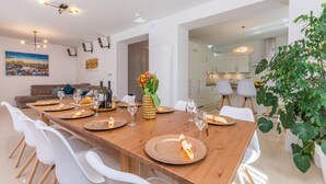 Un espace de salle à manger moderne avec une table en bois dressée pour six personnes, des chaises blanches et un vase rempli de fleurs.