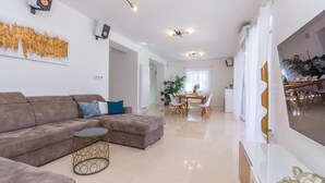 Un salon moderne avec un canapé d’angle, une table basse ronde et un coin repas comprenant une table et des chaises en bois.