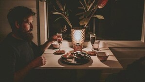A person sitting at a table with a plate of food, a candle, and a vase with flowers.