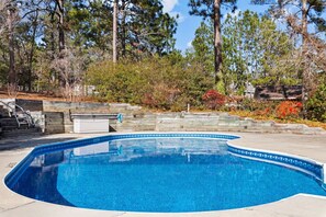 Una piscina con borde curvo, rodeada por una terraza de madera y un muro de piedra.