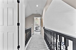 A hallway with a carpeted floor, a white door, and a staircase with black balusters.