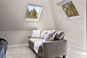 A room with a sofa, two windows, and a carpeted floor.