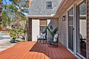 A wooden deck with two chairs and a potted plant, a sliding glass door, and a brick wall.