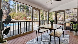 A covered patio with a wooden table, benches, a grill, and a view of trees and a swimming pool. - Southern Pines Getaway w/Hot Tub, Fire Pit & Pool (Southern Pines)
