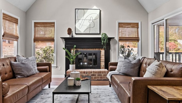 A living room with two leather sofas, a coffee table, a fireplace, and large windows with blinds. - Southern Pines Getaway w/Hot Tub, Fire Pit & Pool (Southern Pines)