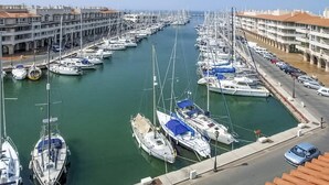 Un port de plaisance où de nombreux bateaux sont amarrés le long d’un canal étroit, entouré d’immeubles à plusieurs étages dotés de balcons.