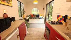 A compact kitchen with a dining area, a window with a view, and a small seating area. - Tiny -Eco House -Kokoro.  COMPLIMENTARY ROMANTIC PACKAGE worth $75 -OTWAYS LORNE (Benwerrin)