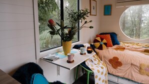 A cozy bedroom with a bed, a desk, and a window with a view of trees. - Tiny -Eco House -Kokoro.  COMPLIMENTARY ROMANTIC PACKAGE worth $75 -OTWAYS LORNE (Benwerrin)