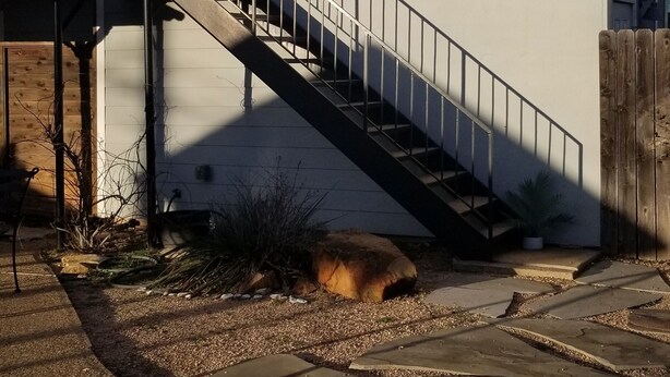 Ett hus med en trappa som leder till ytterdörren, en liten veranda och en trädgårdsdel med en krukväxt och en gång av sten.