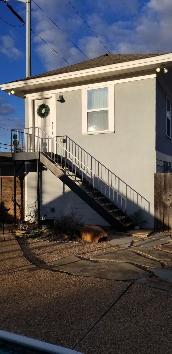 A house with a staircase leading to the front door, a small porch, and a garden area with a potted plant and a stone pathway.