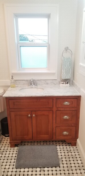 A bathroom with a marble sink, wooden vanity, a window, and patterned floor tiles.