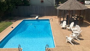 En rektangulär swimmingpool med ett trädäck och vita Adirondack-stolar.