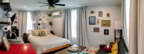 A hotel room with a bed, a desk, a chair, a coffee machine, a ceiling fan, and a window with curtains. - Poolhouse studio, historic neighborhood (Waco)