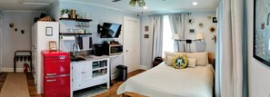 Ein Schlafzimmer mit einem Bett, einem Fernseher, einem roten Kühlschrank, einem weißen Schrank und einem Fenster mit Vorhängen.