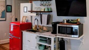 A compact kitchen with a red refrigerator, a microwave, and a coffee maker on a shelf.