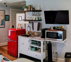 Eine kleine Küche mit einem roten Kühlschrank, einer Mikrowelle und einer Kaffeemaschine auf einem Regal.
