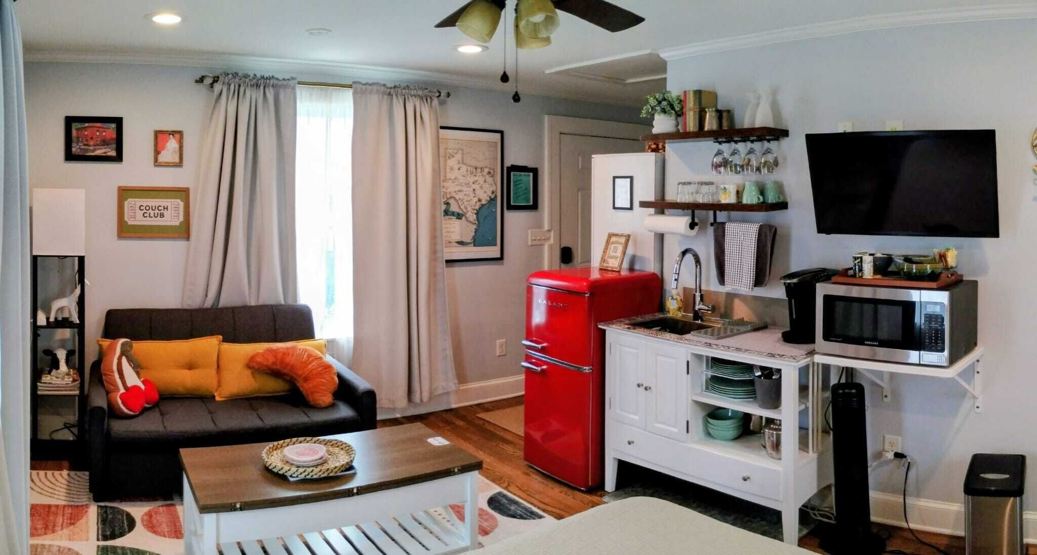 Un espace de vie compact comprenant un canapé, un réfrigérateur rouge, un four à micro-ondes et un téléviseur.