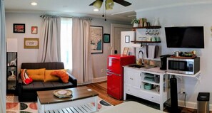 A compact living space with a sofa, a red refrigerator, a microwave, and a television.