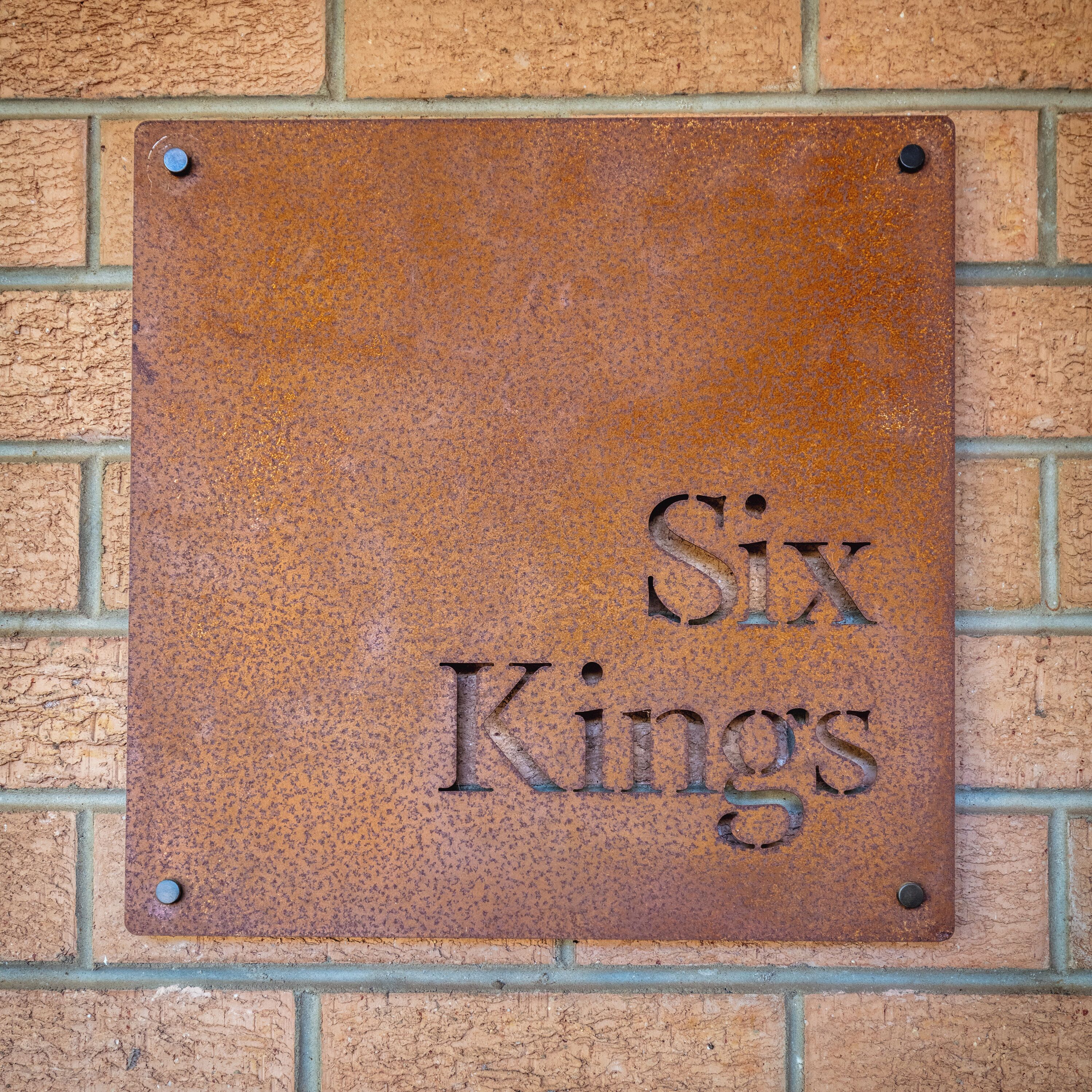 Eine Metallplakette mit der Aufschrift 'Six Kings' an einer Ziegelwand befestigt.