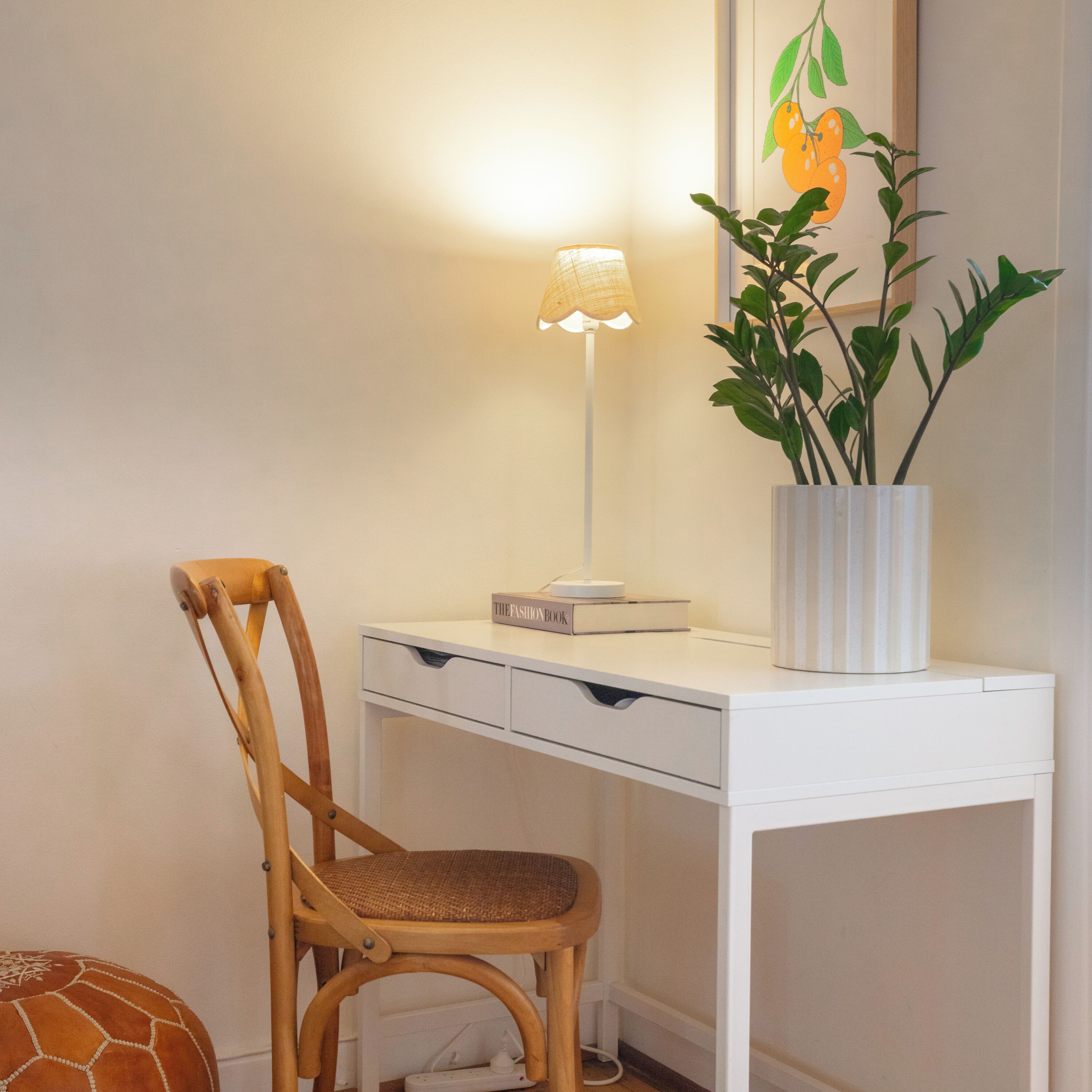 A white desk with a lamp, a book titled "THE FASHION BOOK," and a potted plant.