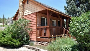 A rustic cabin with a stone chimney, wooden porch, and surrounding greenery. - White Cliffs are Truly a Glorious Sight -Pool -Hot Tub-Breakfast-Farm-Zion/Bryce (Mount Carmel)