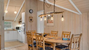 A wooden dining table with six chairs, a clock on the wall, and a kitchen in the background. - Stunning home in Gedser with sauna (Gedser)