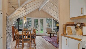 A spacious dining area with a wooden table and chairs, a large window offering a view of the outdoors, and a kitchen area with wooden cabinets and utensils. - Stunning home in Gedser with sauna (Gedser)