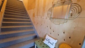 Un escalier avec une rampe, une étagère métallique fixée au mur et un coussin orné de l’inscription « NOTRE invité ».