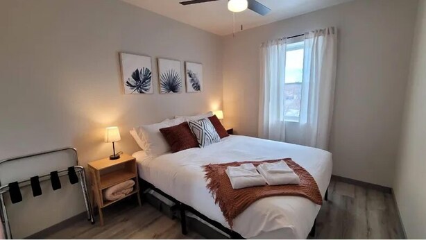 Une chambre à coucher bien rangée, avec un lit, des lampes de chevet, une table de nuit et une fenêtre avec des rideaux.