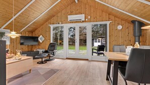 A cozy cabin interior with a wooden ceiling, a TV, a dining table, and a large sliding glass door leading to a deck. - Awesome home in Oksbøl with WiFi (Oksbøl)
