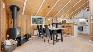 A cozy cabin with a wood-burning stove, a dining area with chairs, a kitchen with cabinets, and a window with a view of trees. - Awesome home in Oksbøl with WiFi (Oksbøl)