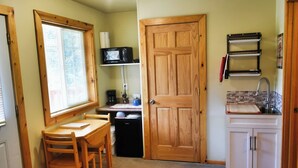 Une cuisine compacte avec une porte en bois, une table à manger avec des chaises, un four à micro-ondes, une machine à café et un évier.