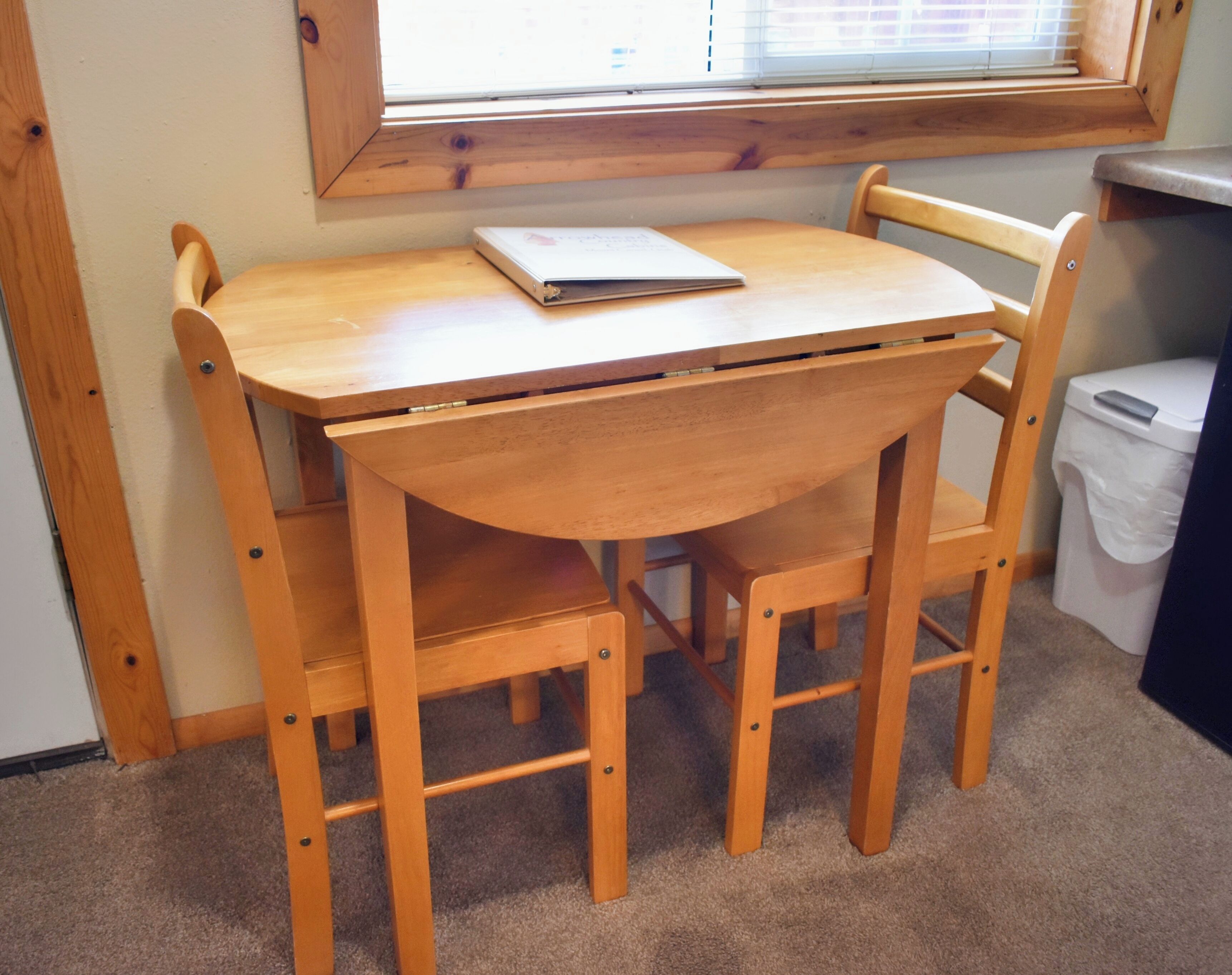 Una mesa de madera con una computadora portátil encima, rodeada por cuatro sillas.