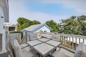 A deck with a table and chairs, a wooden fence, and a blue house in the background.
