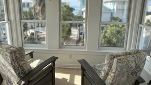 A room with a bay window overlooking a residential area, featuring two wooden chairs with floral upholstery and a wooden bench. - Newly Remodeled. 20 second walk to Beach walkover. Gulf views on 2nd/3rd floors! (Panama City Beach)