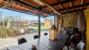 Un patio al aire libre con una mesa de madera, sillas, una parrilla y un muro de piedra.