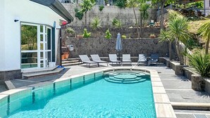 Ein Schwimmbecken mit klarem Wasser, umgeben von Liegestühlen und Blumentöpfen.