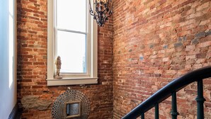 A staircase with a brick wall, a window with a decorative item, and a hanging light fixture. - YOUR URBAN OASIS - Paristown, Downtown, Highlands, NULU - brand new!! (Louisville)