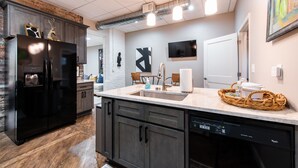 A modern kitchen with dark cabinets, a black refrigerator, a built-in dishwasher, and a large island with a sink. - YOUR URBAN OASIS - Paristown, Downtown, Highlands, NULU - brand new!! (Louisville)