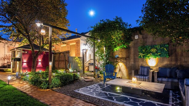 A well-lit patio area with a brick pathway, outdoor furniture, and a decorative wall. - YOUR URBAN OASIS - Paristown, Downtown, Highlands, NULU - brand new!! (Louisville)