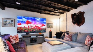 A living room with a large flat-screen TV, a mounted animal head, and a cozy seating arrangement. - YOUR URBAN OASIS - Paristown, Downtown, Highlands, NULU - brand new!! (Louisville)