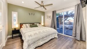 Ein Schlafzimmer mit Bett, Deckenventilator, Nachttisch, Fenster und Blick ins Freie.