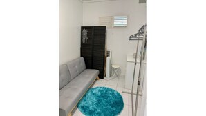 A small, compact room with a grey sofa, a blue rug, a wardrobe, a small table, and a radiator. - Welcome to the heart of my island (Schoelcher)