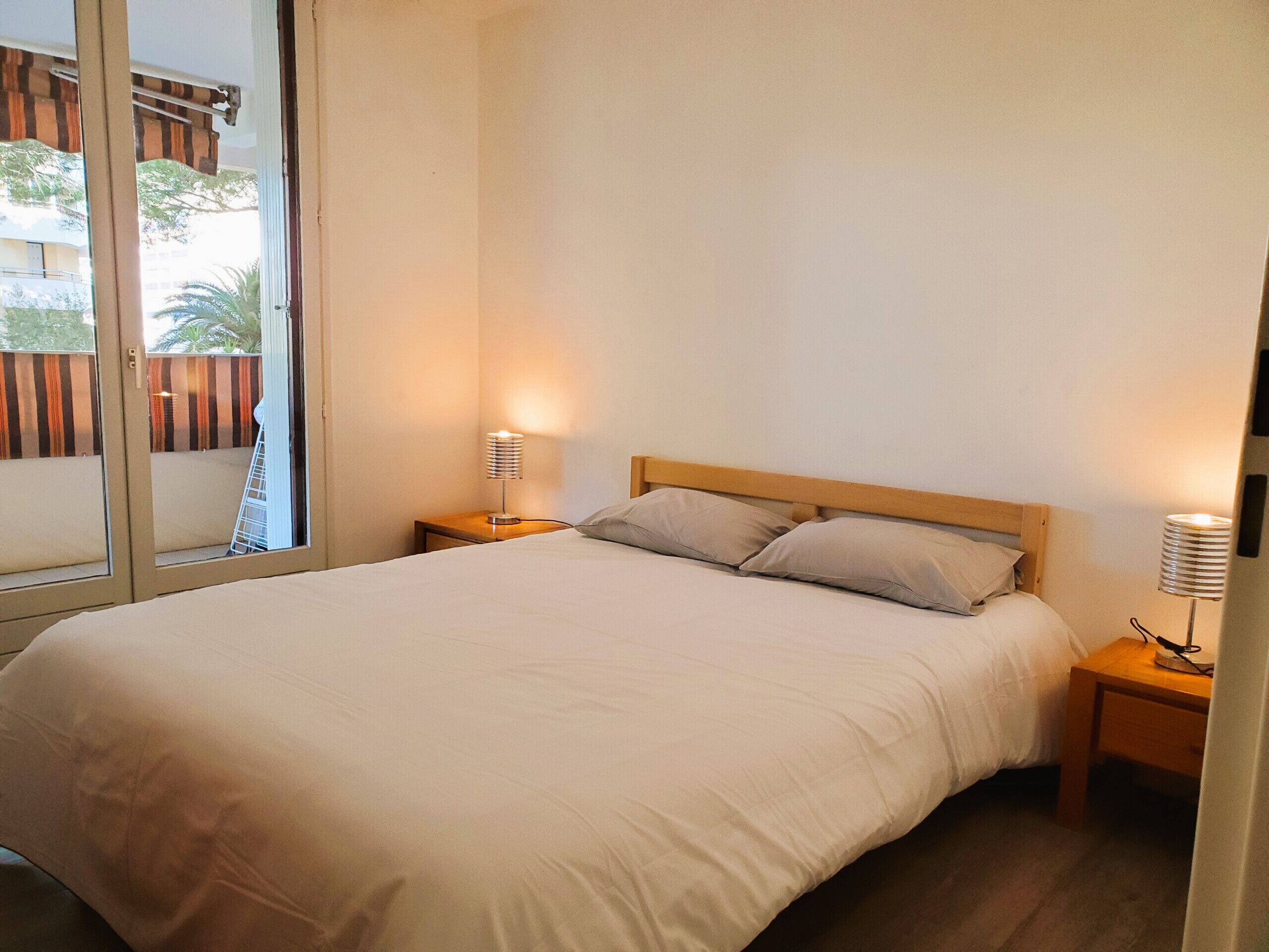Uma cama bem arrumada com duas almofadas, uma cabeceira de madeira e duas luminárias de cabeceira.