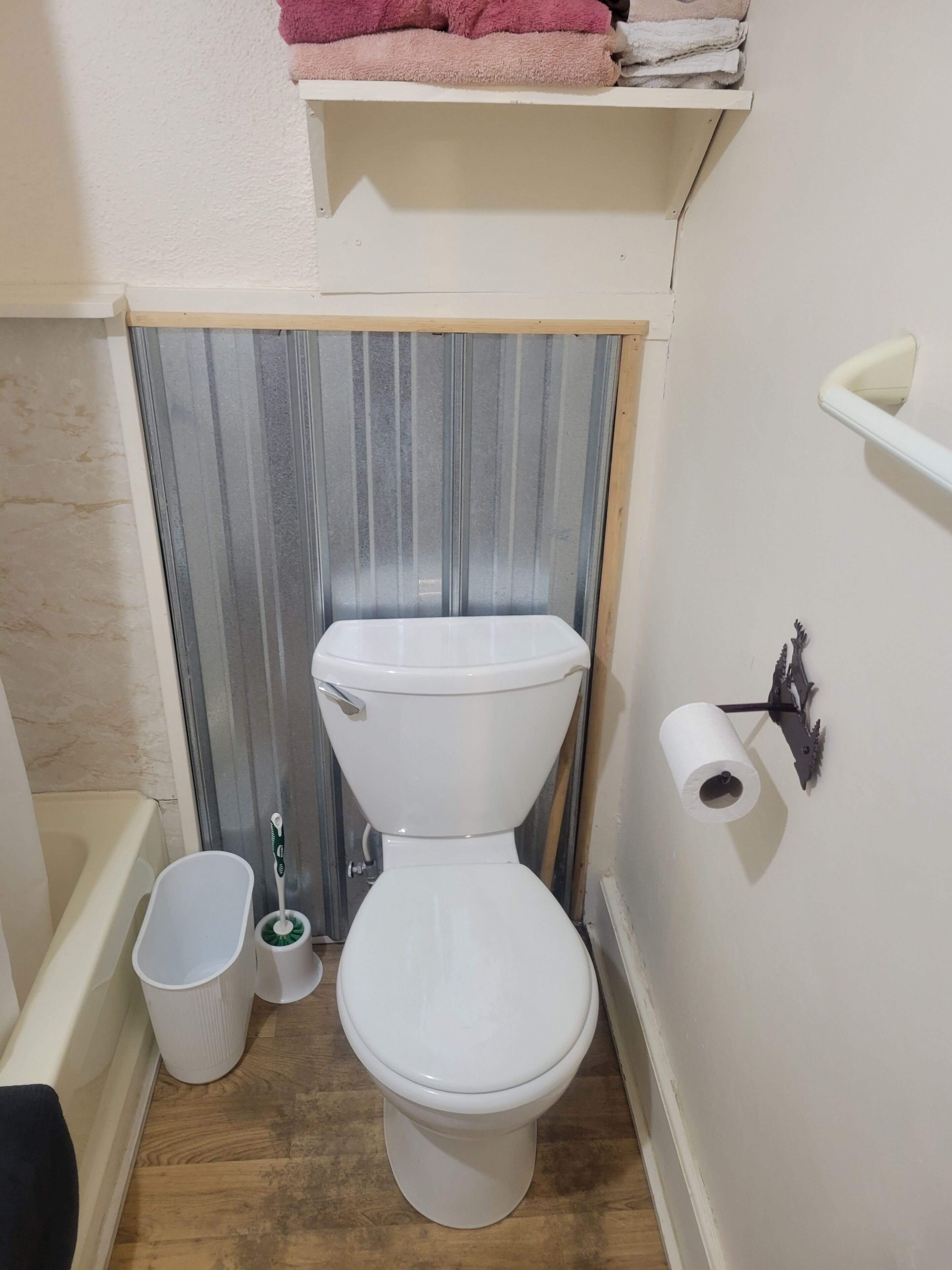 A small bathroom with a toilet, a trash bin, and a toilet brush.